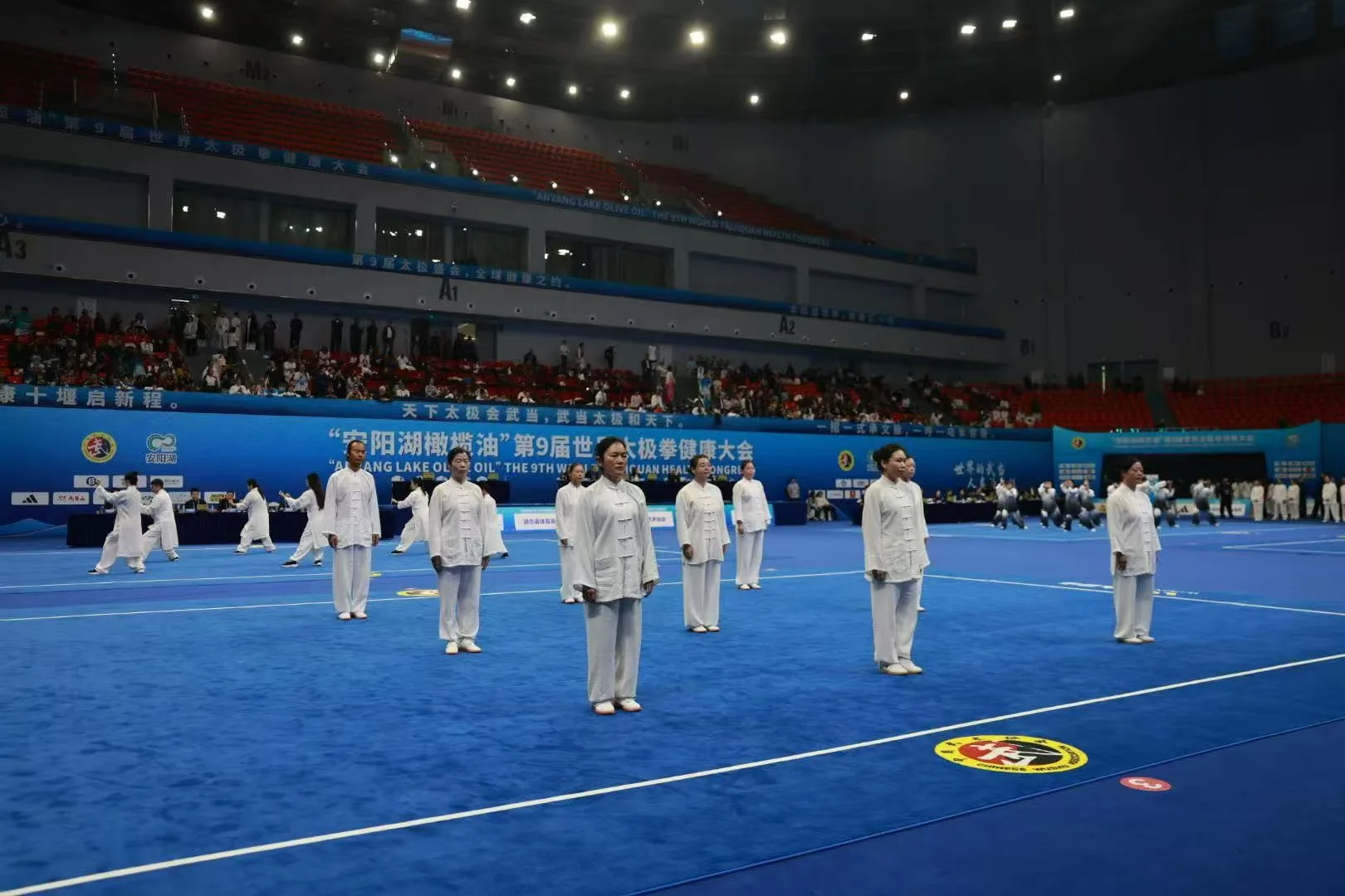 The team stands in formation on a blue competition mat in a large arena.
