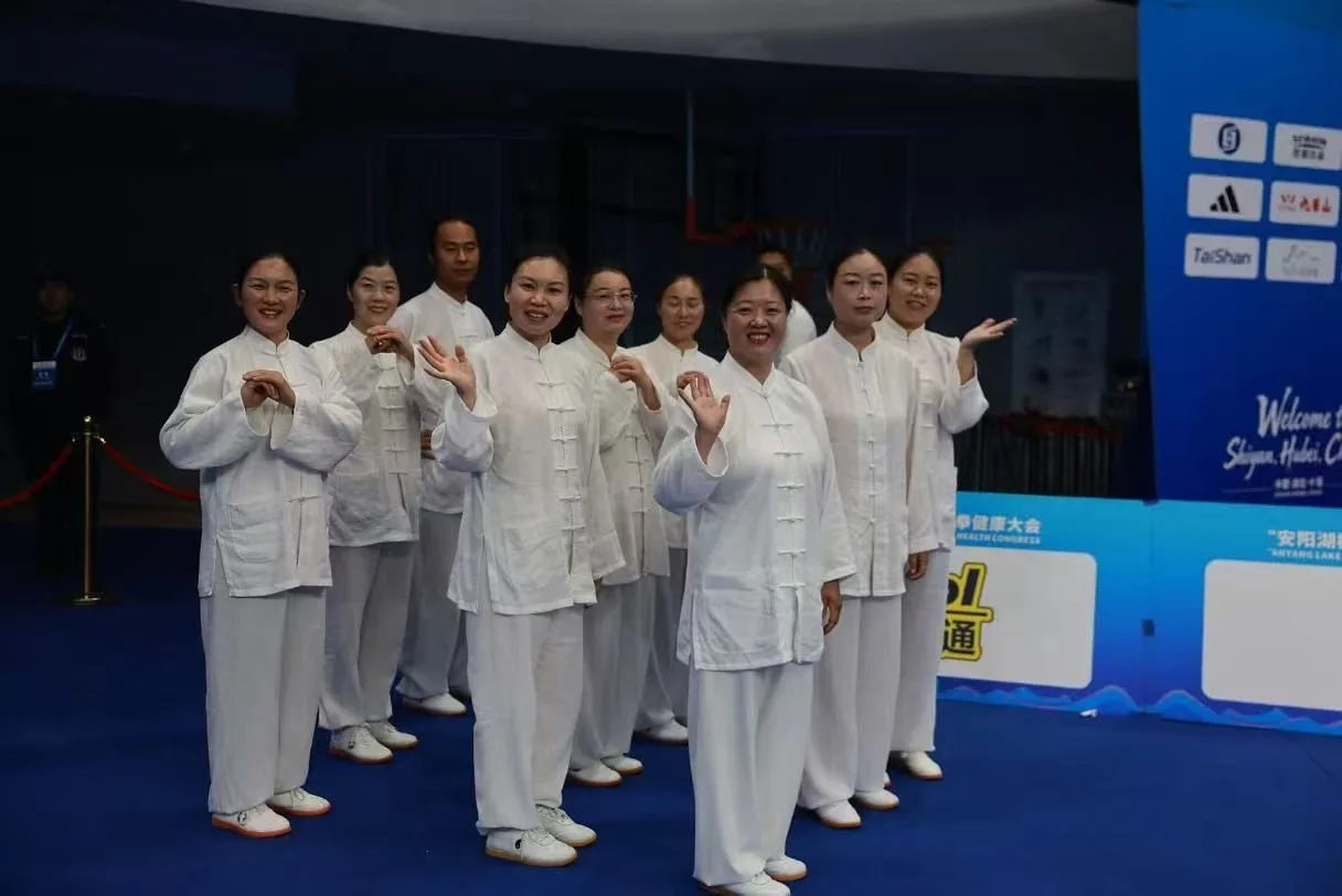 Practitioners in white taiji uniforms wave and smile at the edge of the arena.