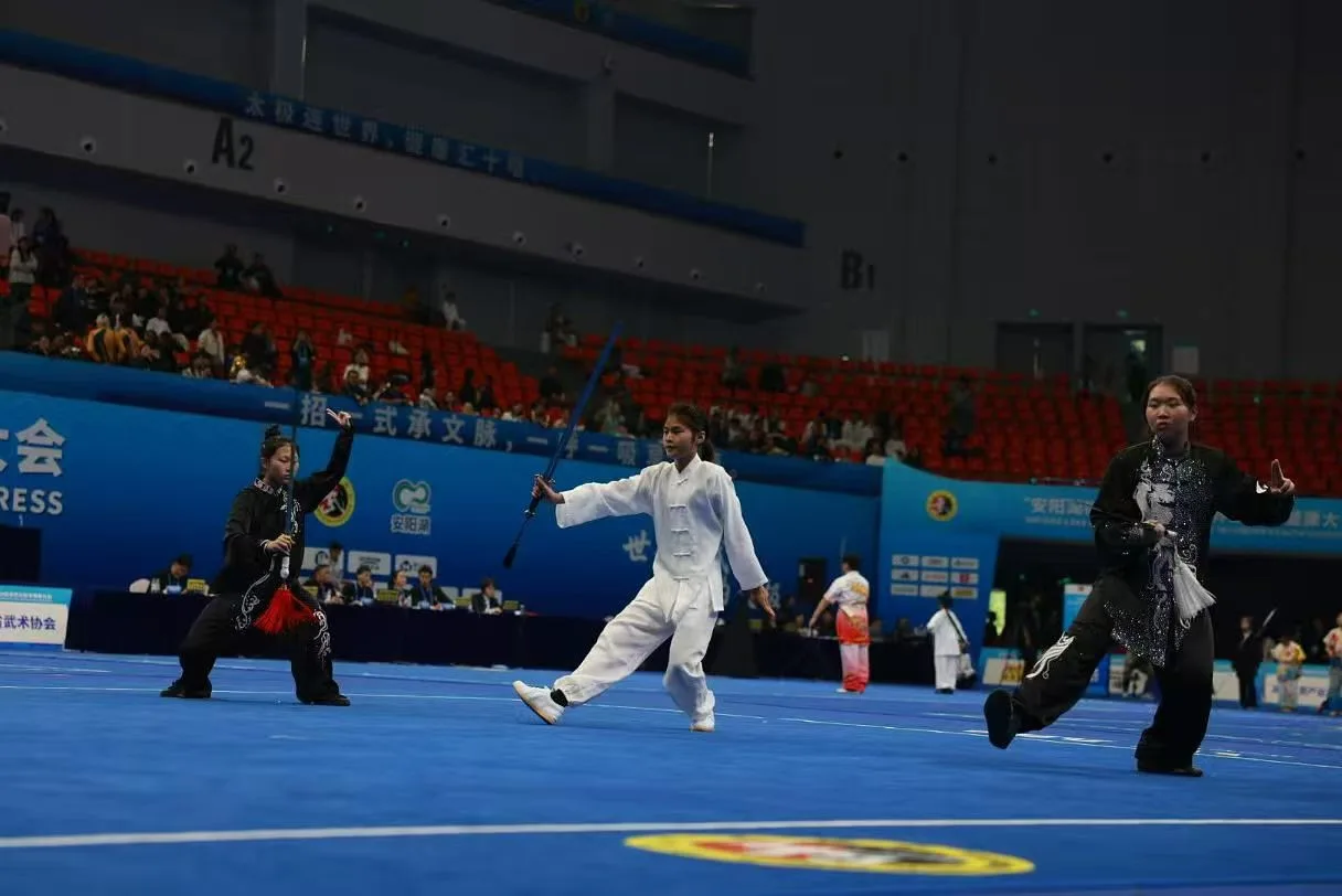 A young practitioner in white performs with a long weapon, with competitors in black on either side.