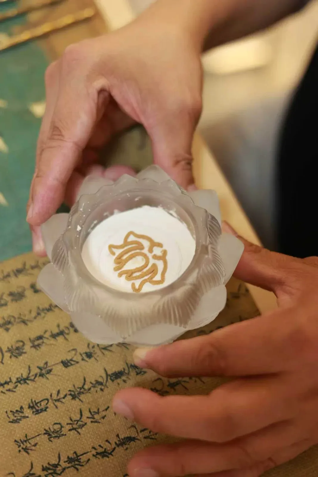 Une ligne continue de poudre d’encens dorée dessine un sceau sur la cendre blanche d’un brûle-parfum en forme de lotus.