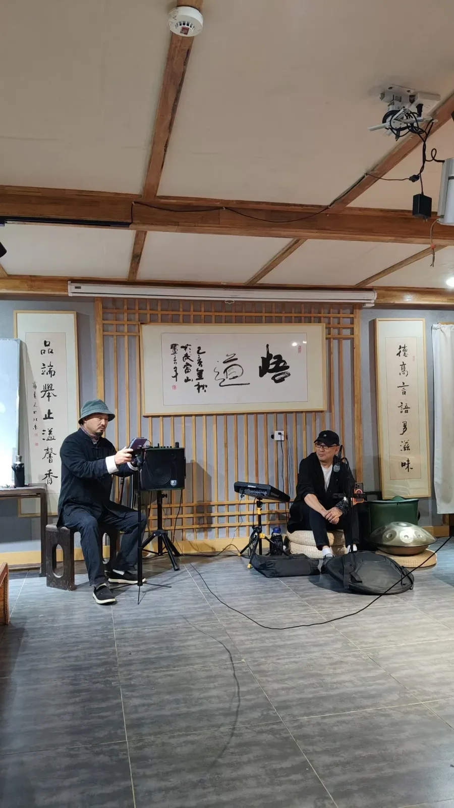 Deux musiciens en noir sont assis devant la calligraphie 悟道 et un couplet, avec un clavier Roland, une enceinte et un handpan.