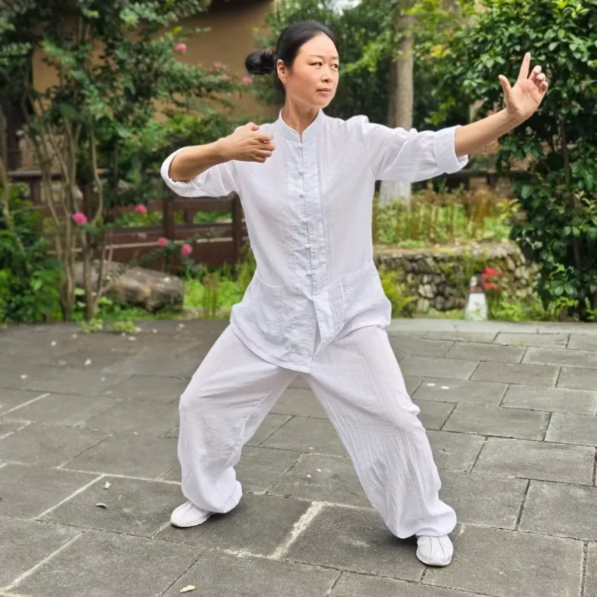 Une personne vêtue de blanc tient une posture basse dans une cour de Wudang.