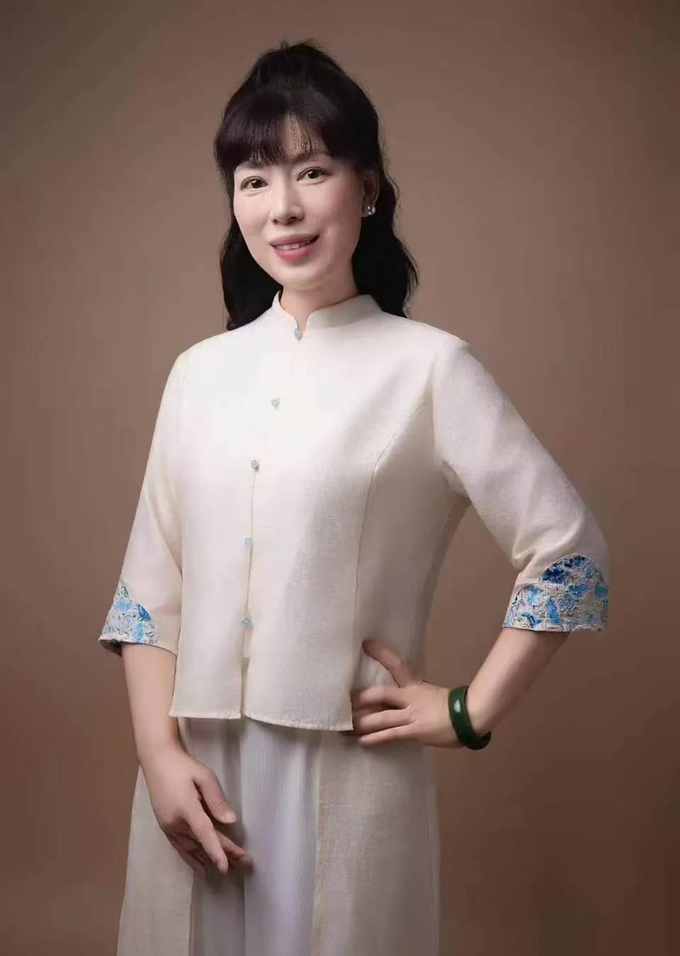 Zhen Ruofei in a cream embroidered jacket, hand on her hip, against a plain brown background.