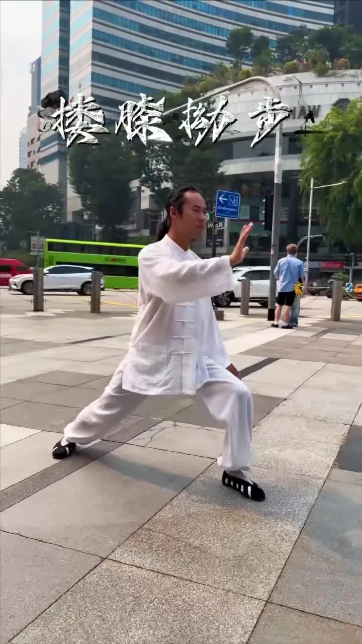 Un homme en blanc tient une posture de tai-chi sur Orchard Road, une paume levée, devant des tours, un bus vert et l’enseigne Shaw House.
