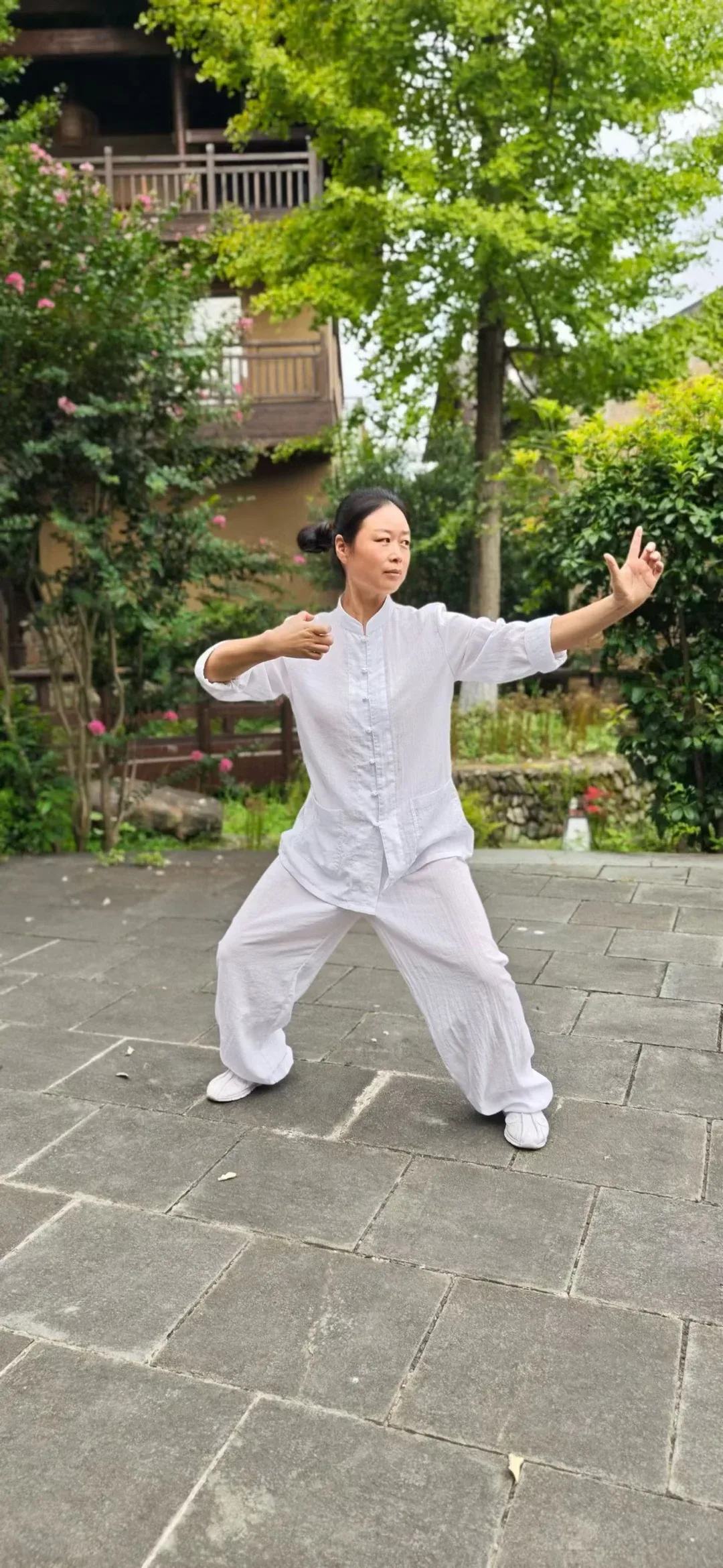 Une personne en blanc tient une posture basse dans la cour pavée, une main ramenée et l’autre tendue, les doigts relevés.