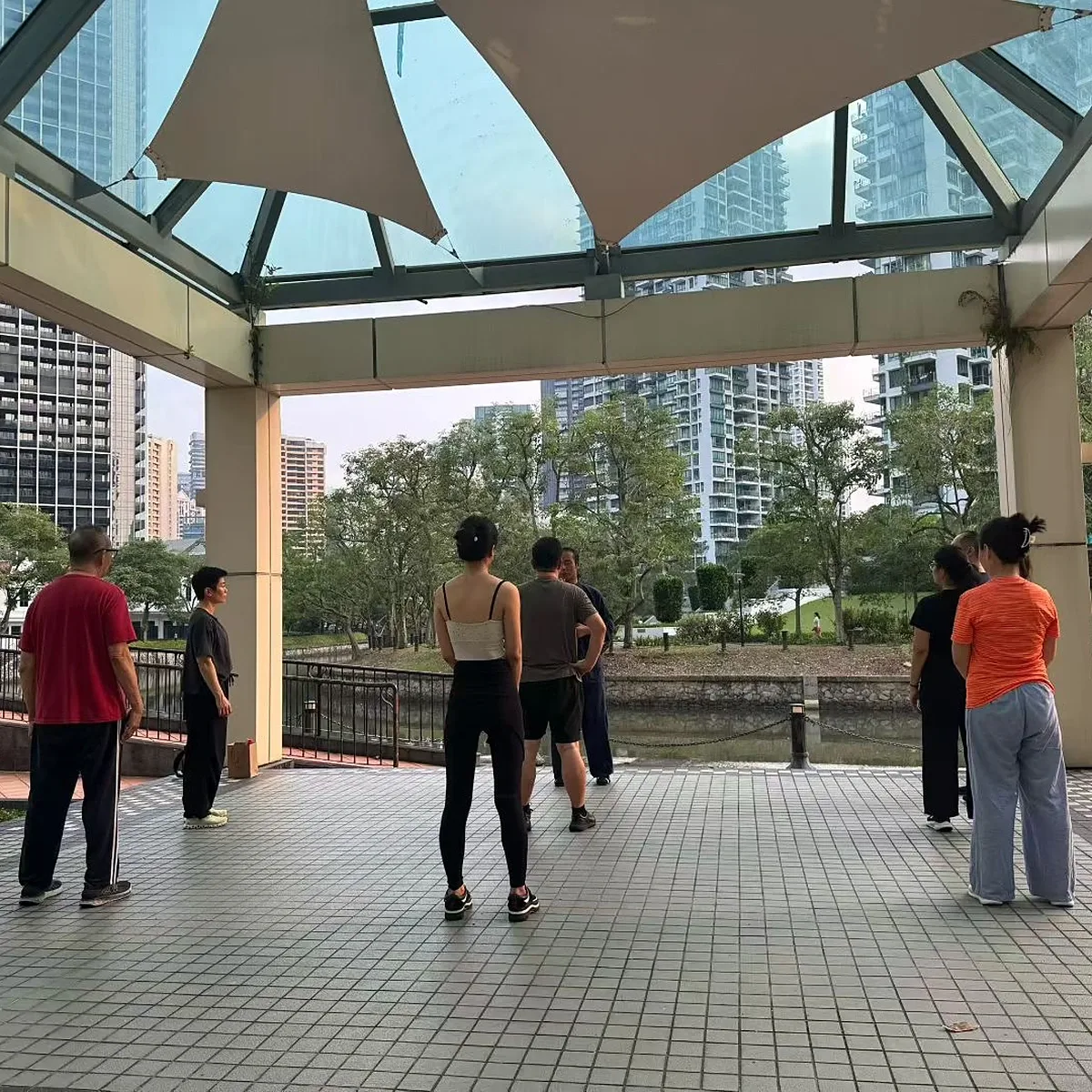 Une séance matinale sous un pavillon au toit vitré et couvert de toile, avec les immeubles de la ville au-delà de la rivière.