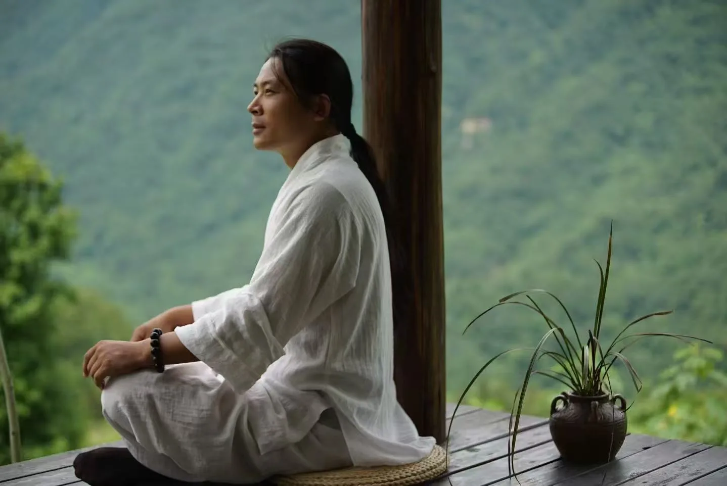 Teacher Lu sits in quiet meditation on a mountain terrace, overlooking forested peaks.