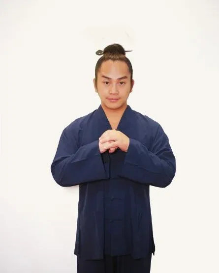 Teacher Sanyuan in a navy Daoist robe, hands held together at the chest