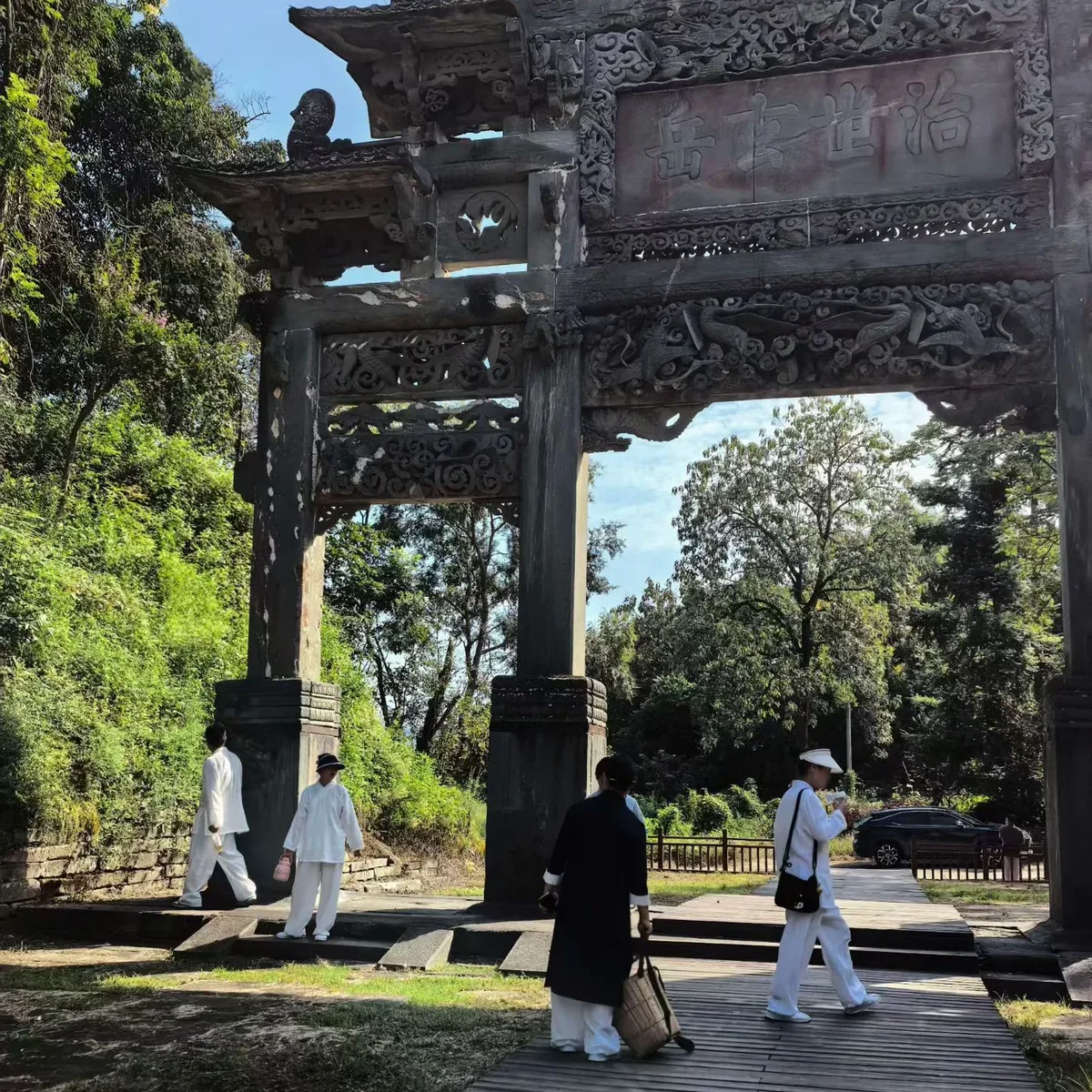 Des marcheurs vêtus de blanc passent sous l’arche de pierre sculptée 治世玄岳 à Wudang.