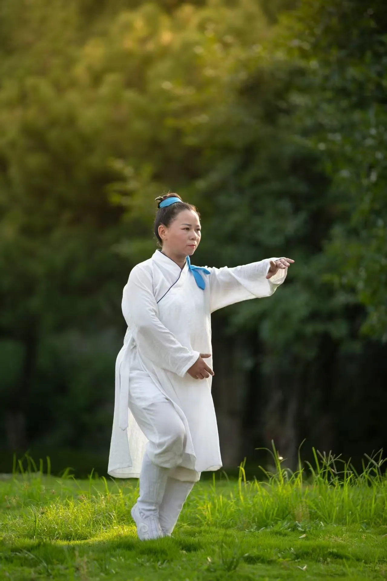 Senior Sister Jiang Sanjiang practises a taiji posture on a lawn in the evening light.