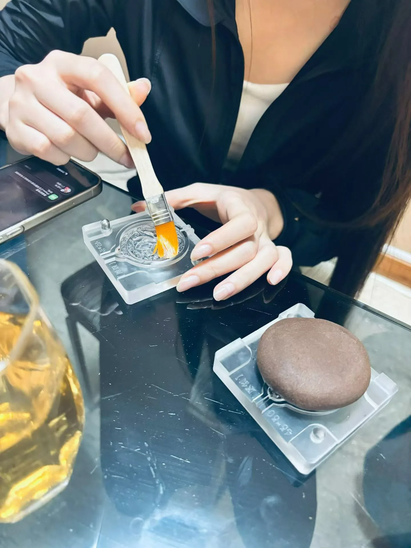 Une participante brosse l’intérieur d’un moule transparent ; un disque de pâte d’encens brune attend dans un second moule.