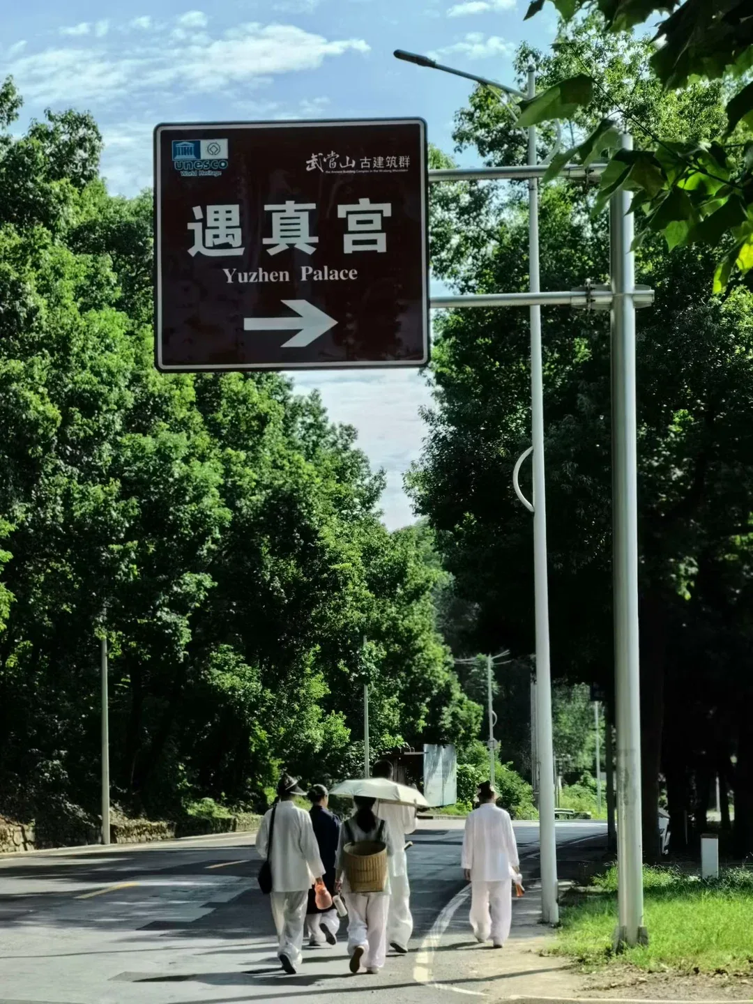 Un groupe en blanc marche sous un panneau patrimonial brun indiquant le palais Yuzhen, 遇真宫, sur la droite.