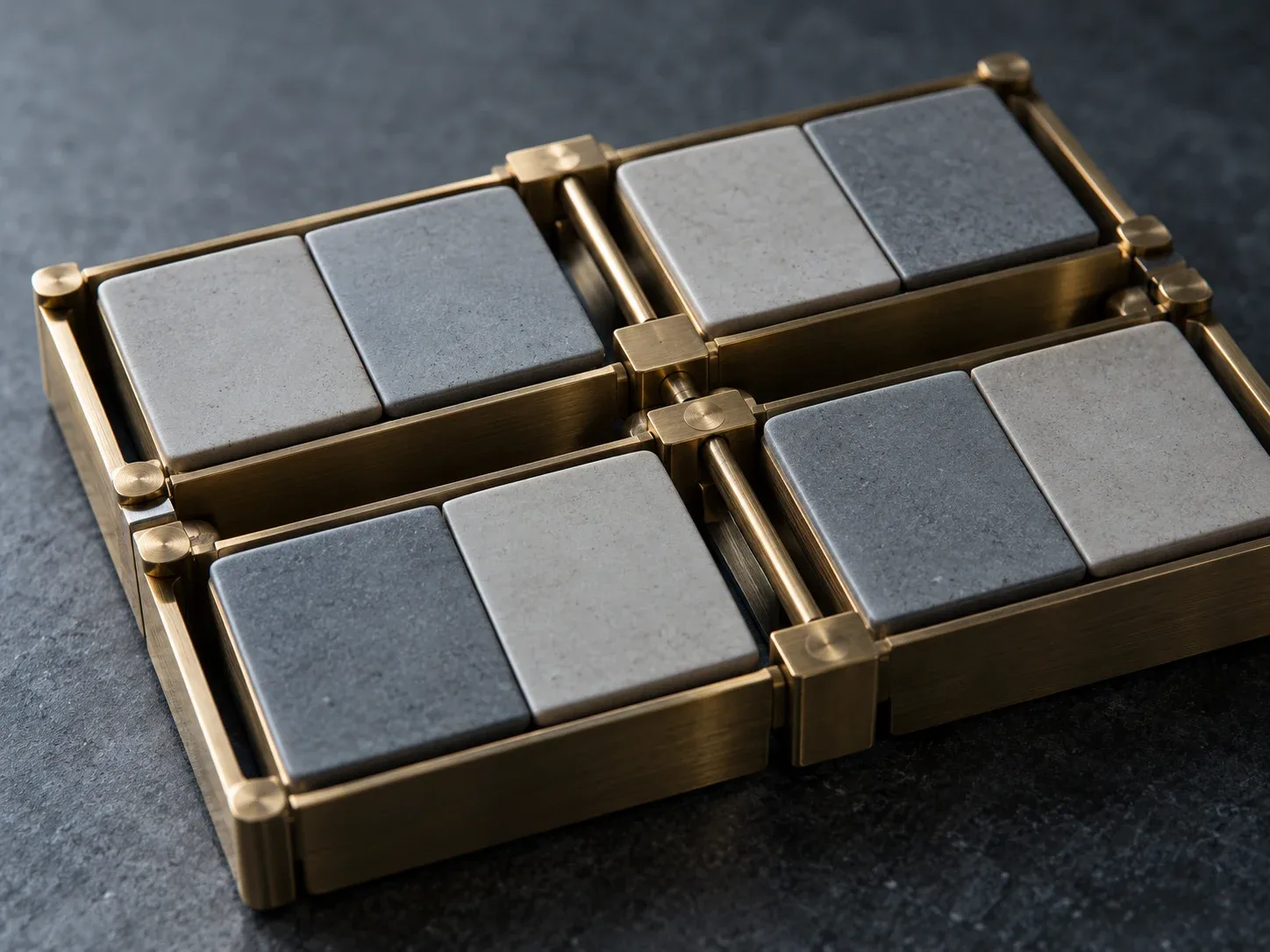 Close view of a modern brass frame holding eight blank ceramic tiles in four paired modules, photographed in cool blue-grey light.