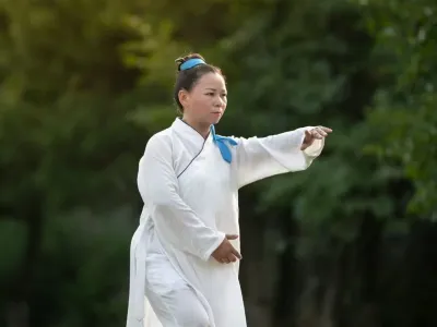 Senior Sister Jiang Sanjiang practises a taiji posture on a lawn in the evening light.